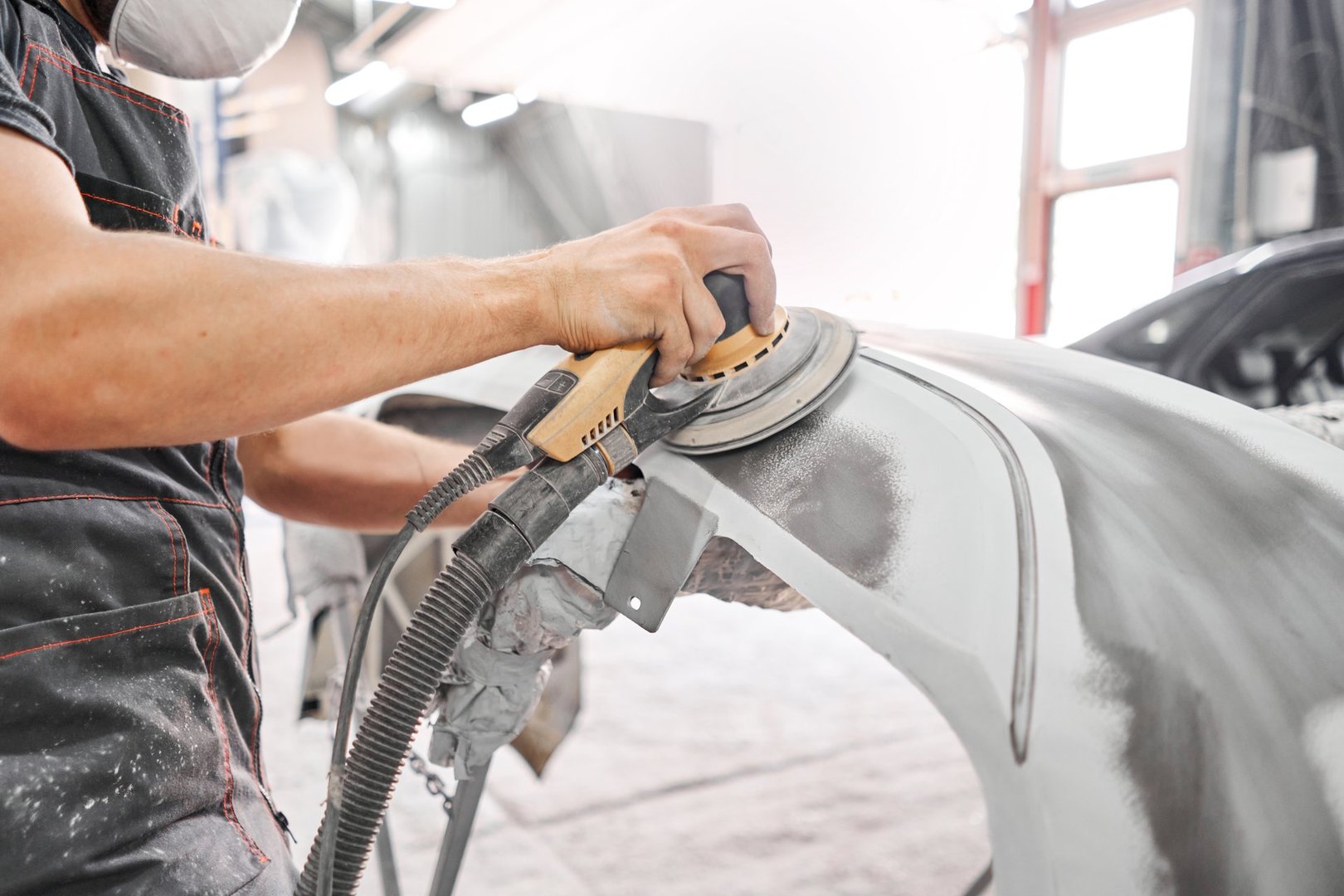 The mechanic works with a grinding tool. Sanding of car elements. Garage painting car service. Repairing car section after the accident